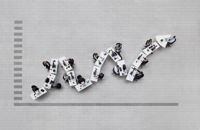 Overhead view of office desks arranged to look like increasing trend on graph