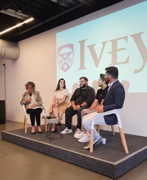 Five people sit on a stage with the Ivey logo in the background