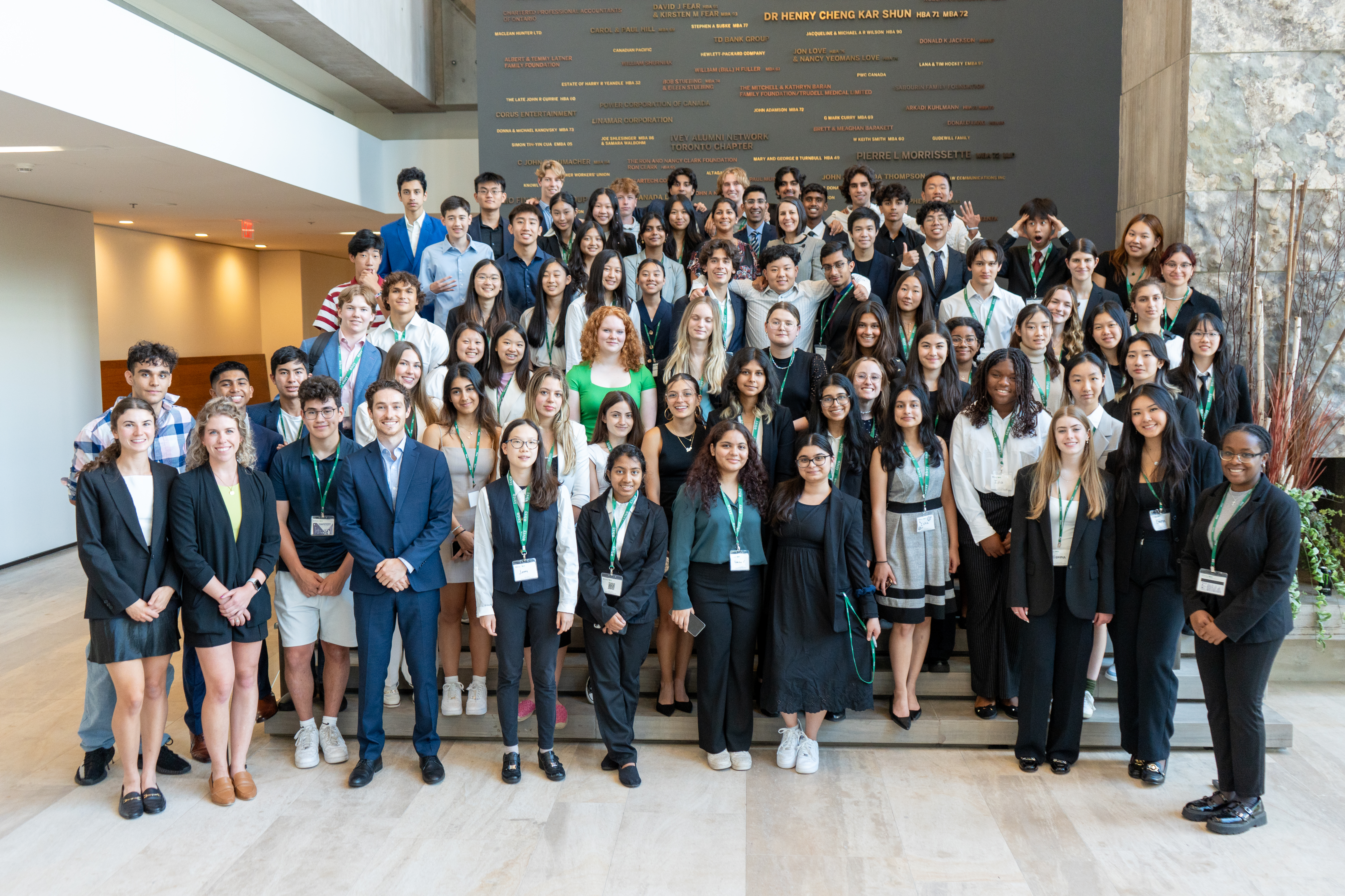 A group of 76 high school students, all wearing business attire, on the main steps in the Ivey Building in front of the Ivey Donor Wall.