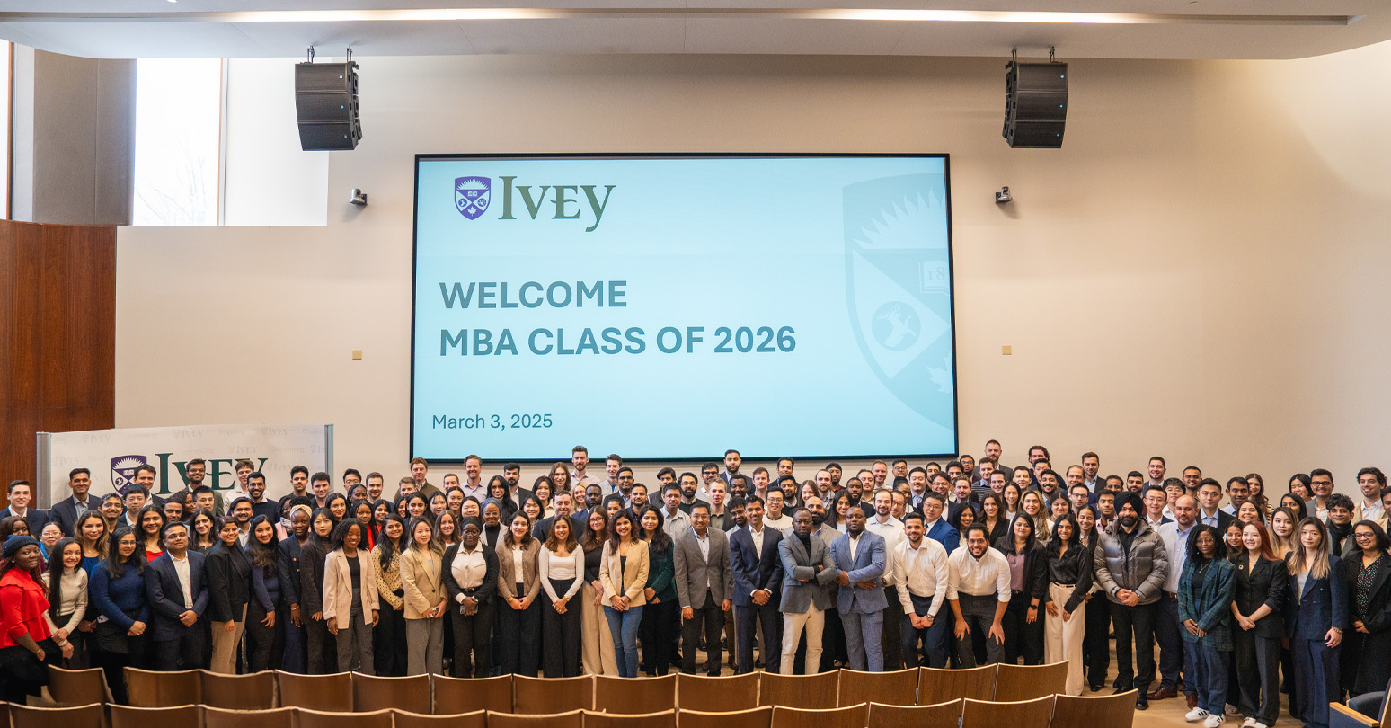 The MBA Class of 2026 students standing in front of a screen that says Welcome MBA Class of 2026