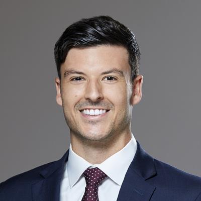 Headshot of Ivey student David Booth. Grey background, David is wearing a blue suit with a white shirt and a dark red tie with white polka dots. The photo is from the shoulders up.