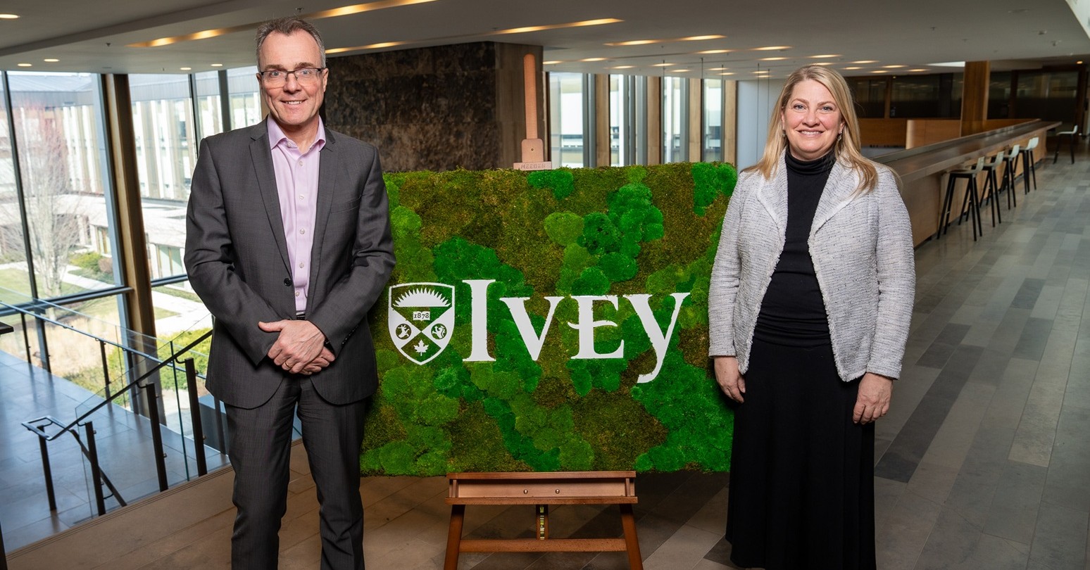 Julian Birkinshaw and Stephanie Brooks standing beside an Ivey sign with a greenery background