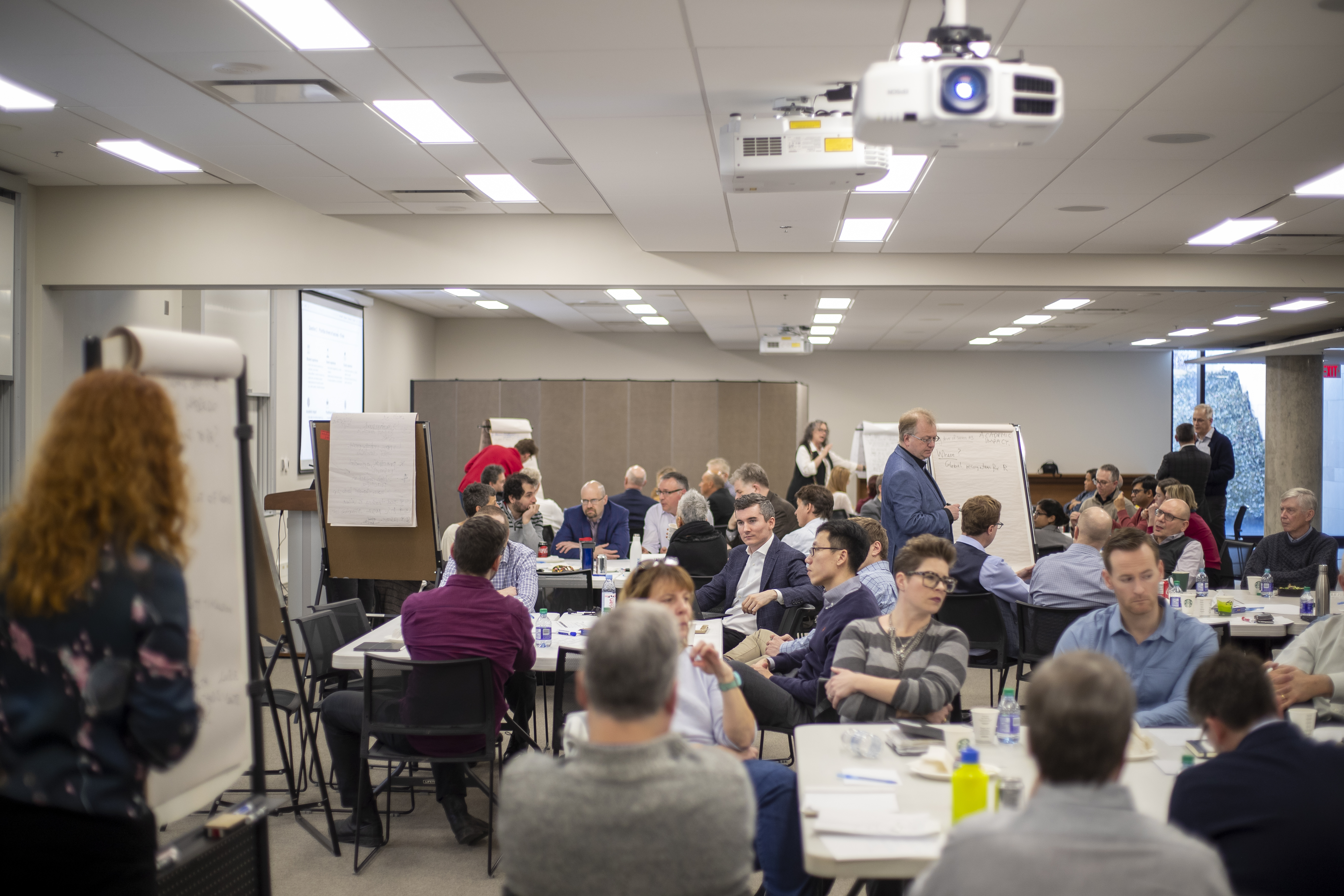 Ivey faculty gathered around tables, collaborating with flip charts for interactive discussion